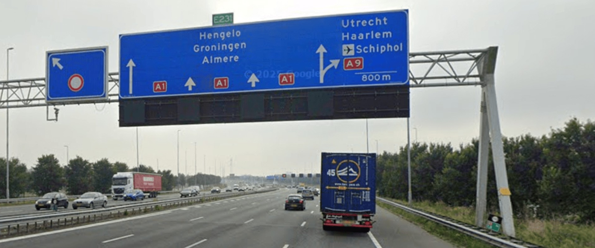 ANWB bord van de A1 boven de snelweg. Op de weg rijden auto's en vrachtauto's. 