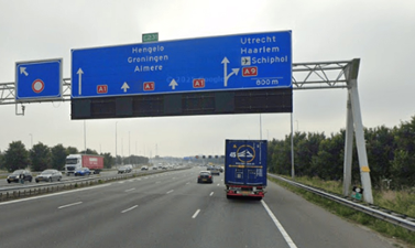 ANWB bord van de A1 boven de snelweg. Op de weg rijden auto's en vrachtauto's. 