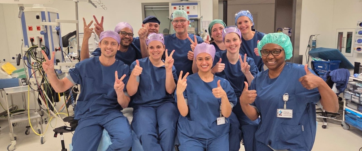 Op de operatiekamer in het ZMC poseert het team met chirurgen en OK medewerkers lachend voor de camera. Ze steken hun duimen trots in de lucht.