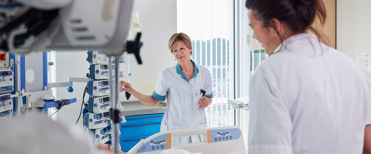 Een verpleegkundige en een arts praten met een patiënt die in bed ligt op de Intensive Care