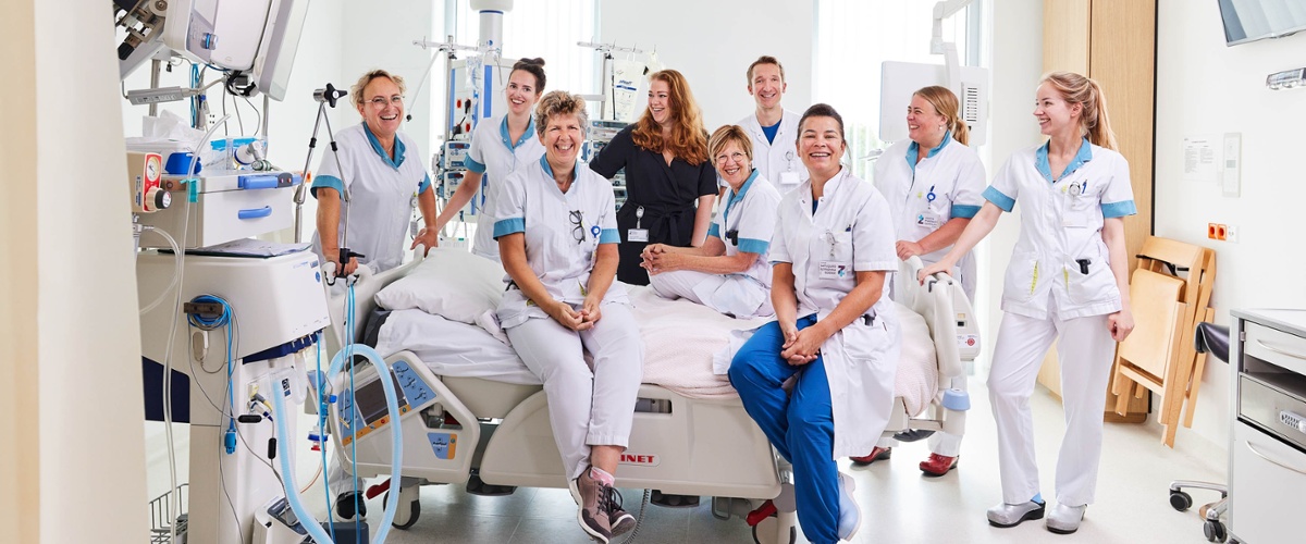Een deel van het team van de Intensive Care zit op en staat naast een bed op de IC.